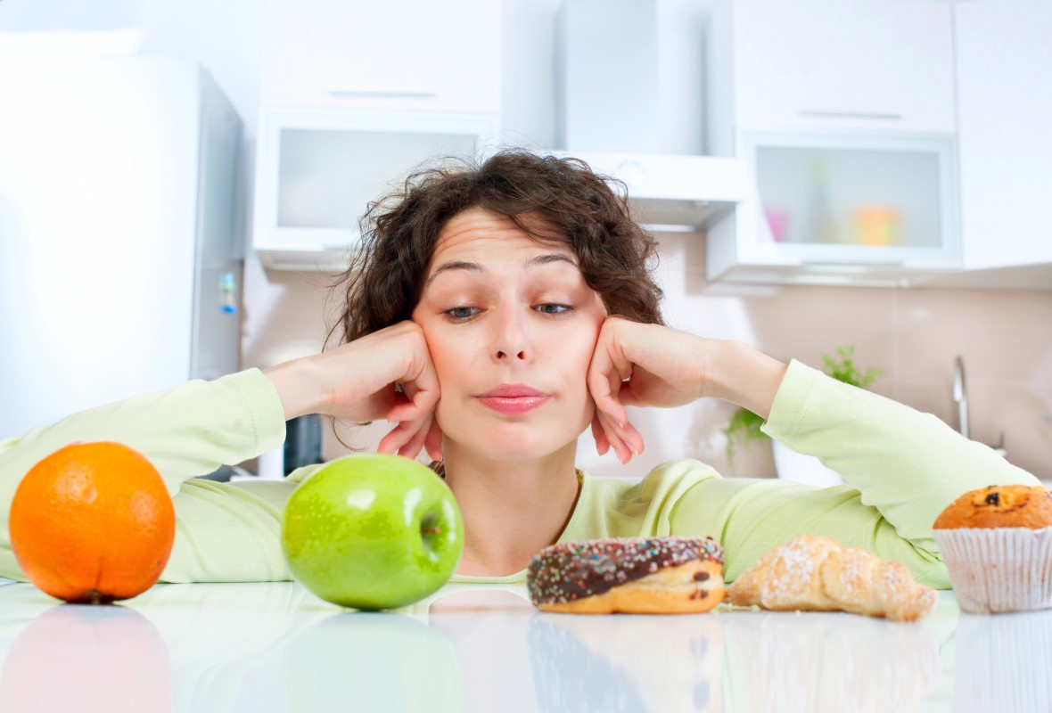 Mujer a dieta intenta decidirse entre comerse una manzana o bollería industrial